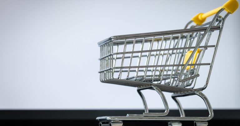 shopping cart on laptop keyboard. White monitor screen with space for text. Concept of online shopping and online stores